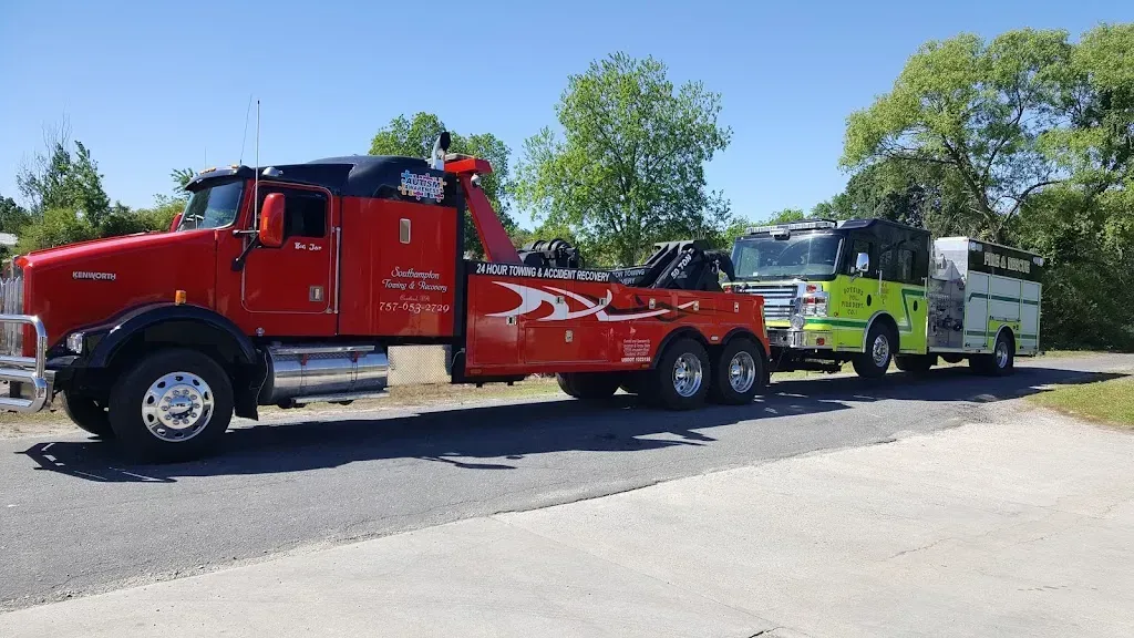 Red tow truck towing a bus and a trailer on a paved road, under a sunny sky.