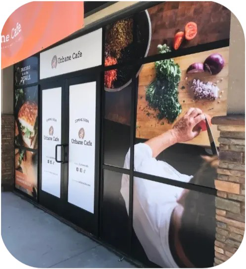 Storefront with large food graphics and signage, showing a worker preparing or serving food inside.