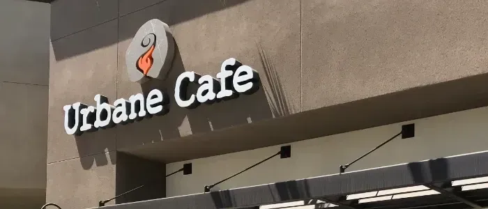 Urbaine Cafe storefront sign on a beige building, with a white coffee cup logo and awning