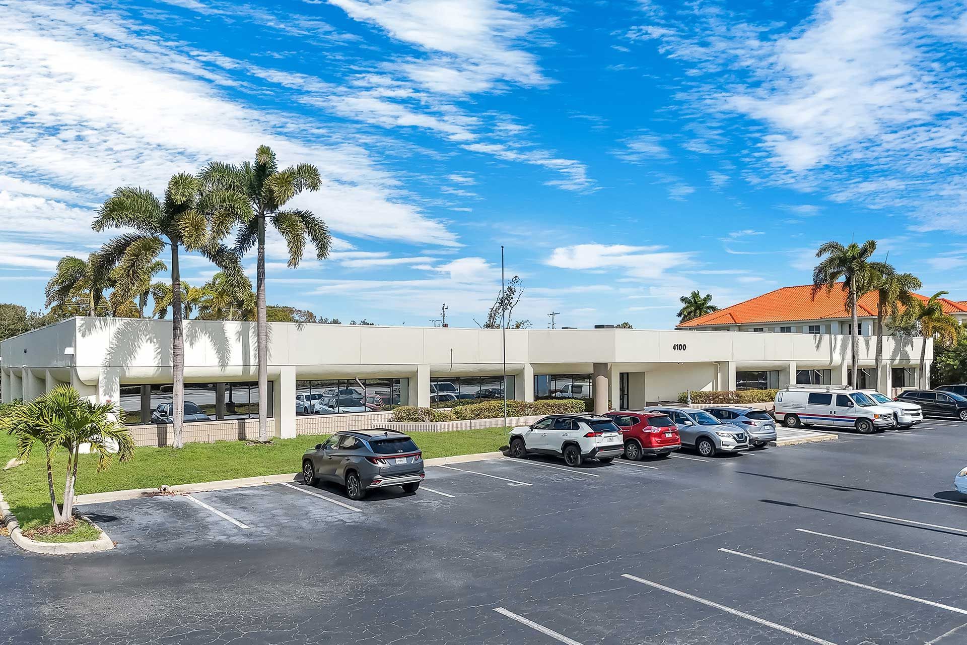 Exterior of a car dealership with cars parked, palm trees, and blue sky.