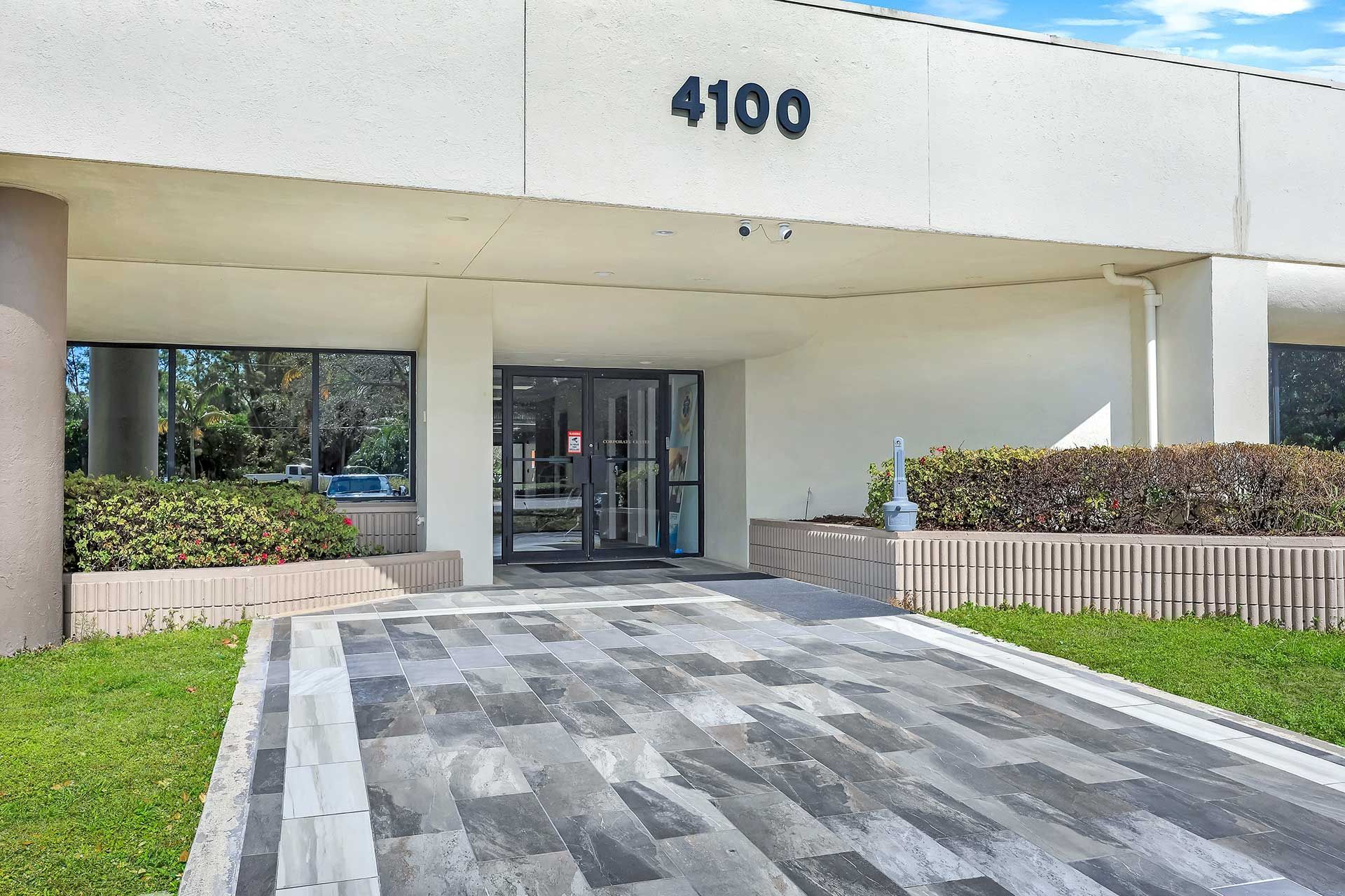 Exterior of a building with the number 4100 above the entrance. Gray walkway leads to glass doors.