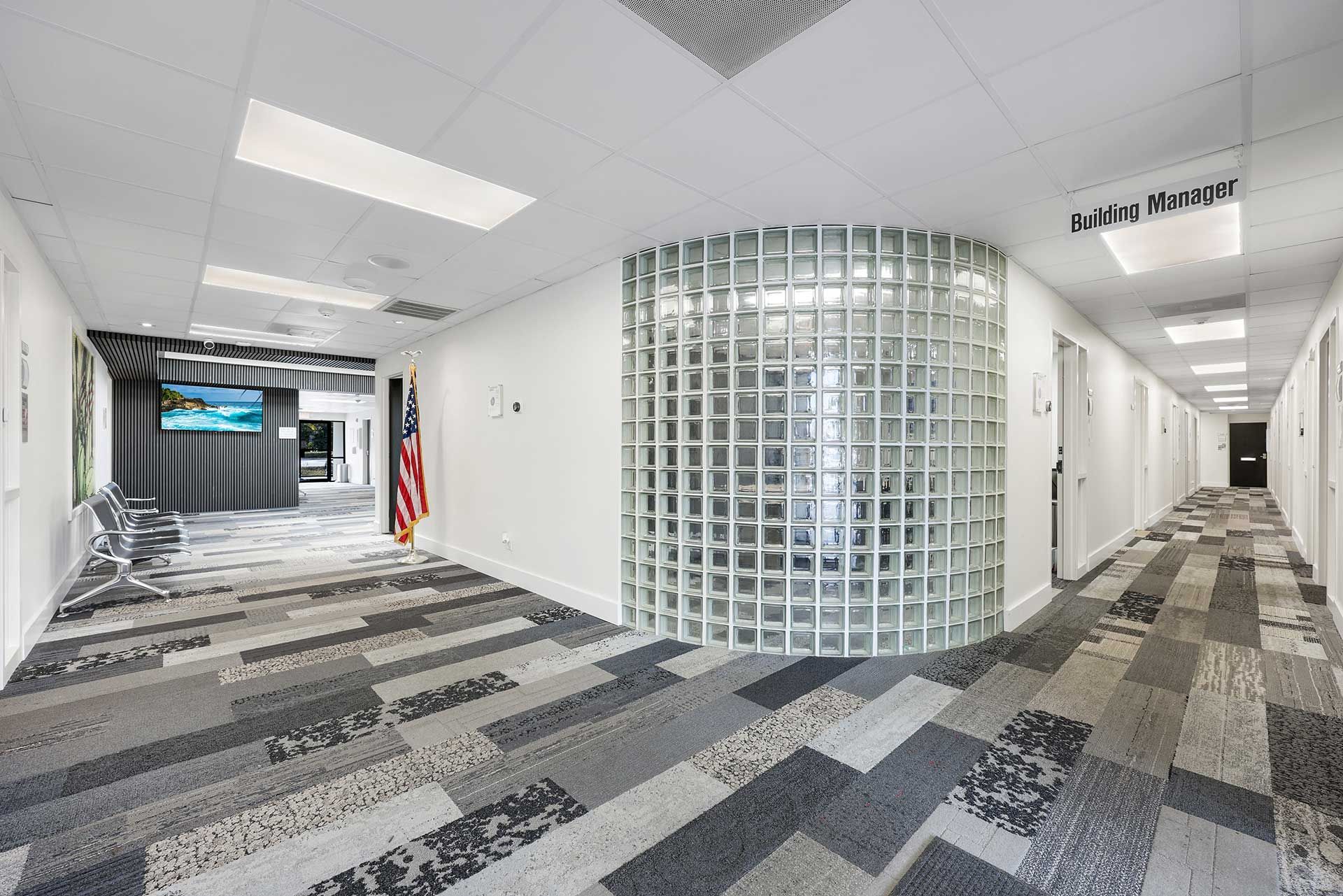Office hallway with patterned carpet, glass block wall, and doors along the right.