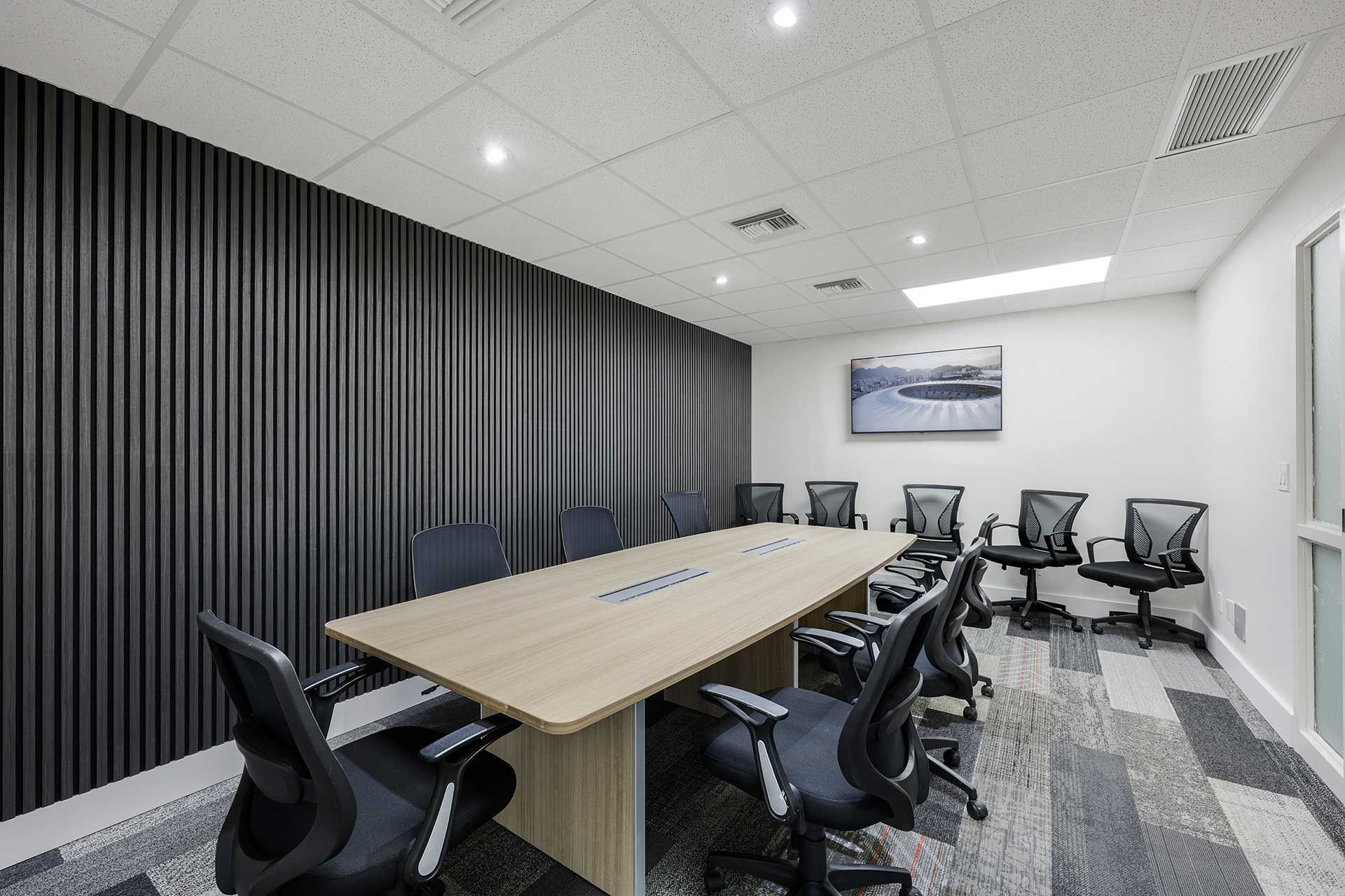 Conference room with long table, black chairs, and dark ribbed wall.