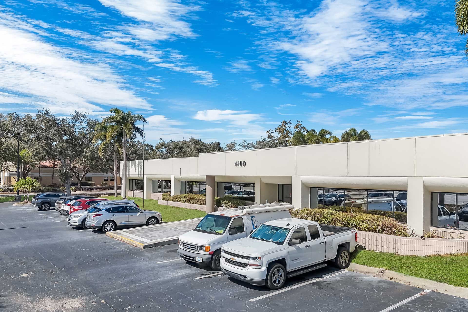 Office building with parking lot and cars under a blue sky with clouds.