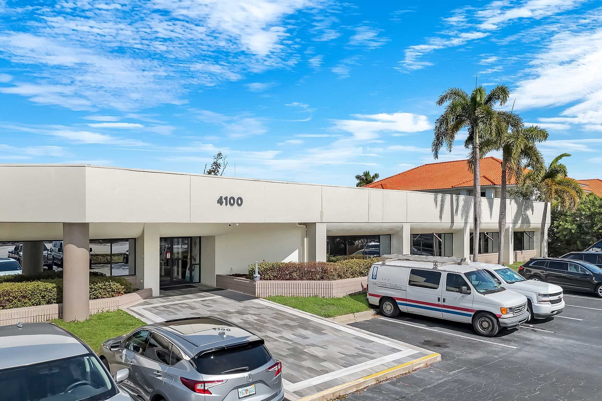 Exterior view of a light-colored commercial building, 4100 above the entrance, with parked vehicles under a blue sky.