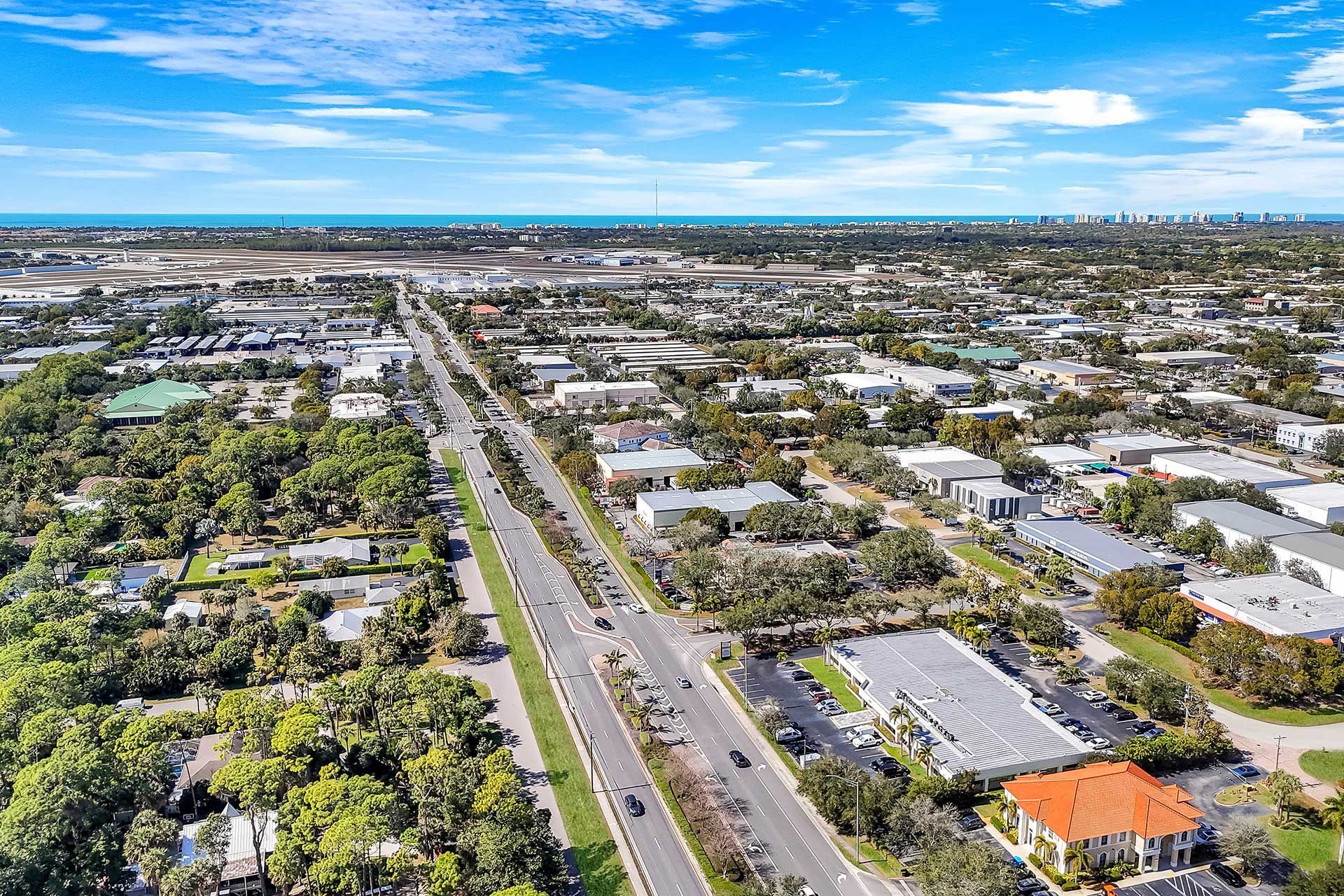 Aerial view of a city street with buildings and lush green trees on a sunny day.