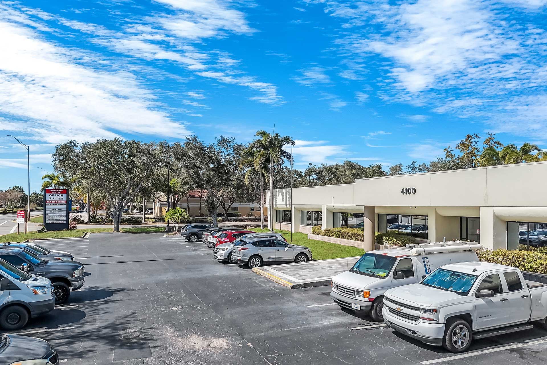 Parking lot with cars in front of a one-story beige building on a sunny day with blue sky.