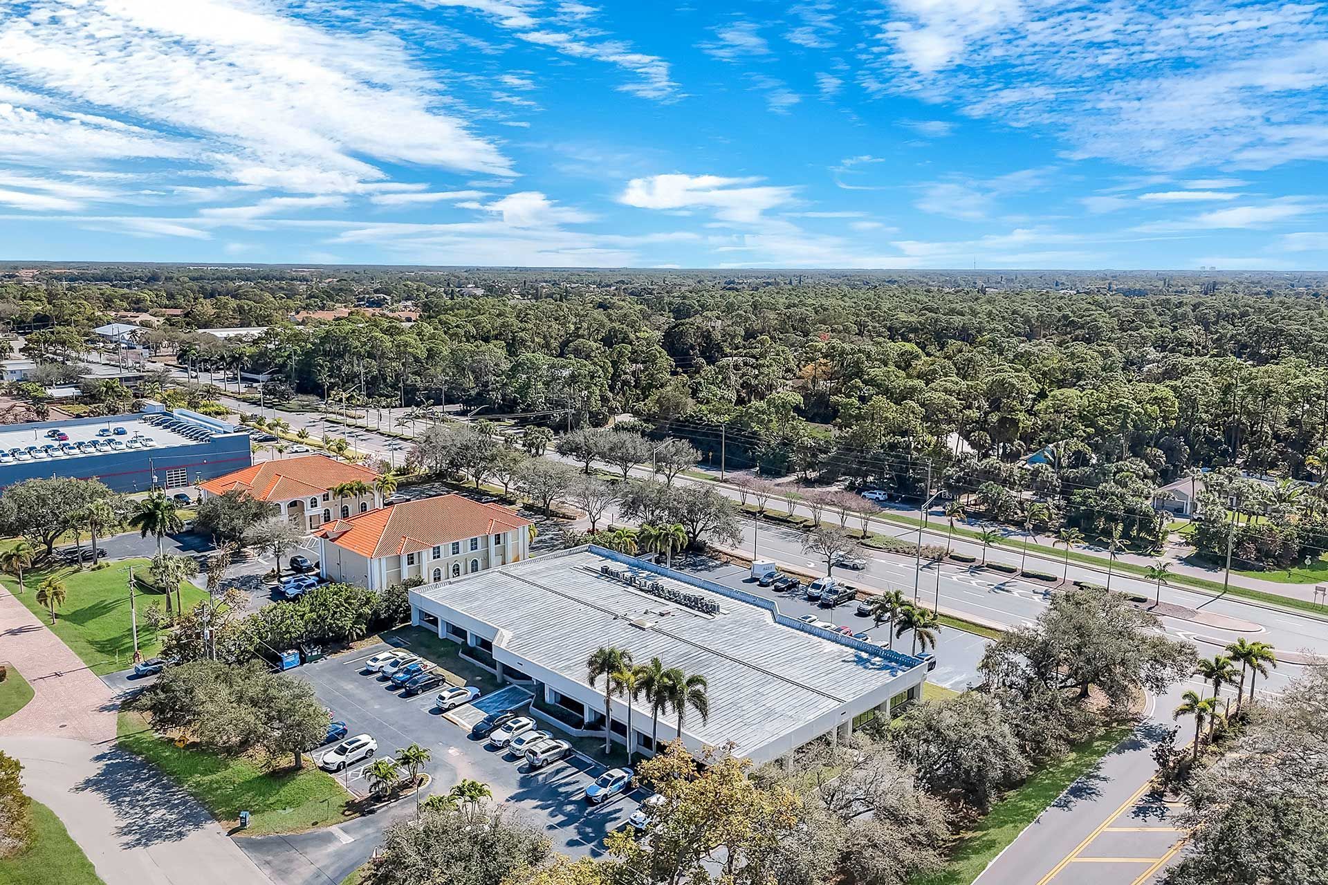 Aerial view of a commercial building with a wavy roof, surrounded by trees and a clear blue sky.