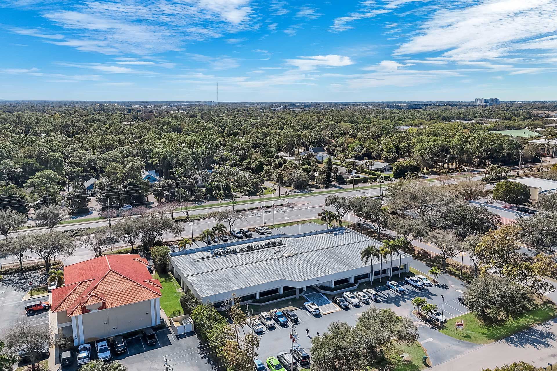 Aerial view of a commercial building with cars parked outside, surrounded by trees and a clear blue sky.