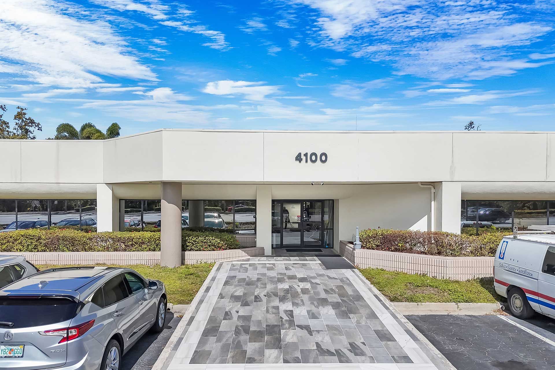 Exterior of a white commercial building, with a paved walkway leading to the entrance. The number 4100 is visible above the door.