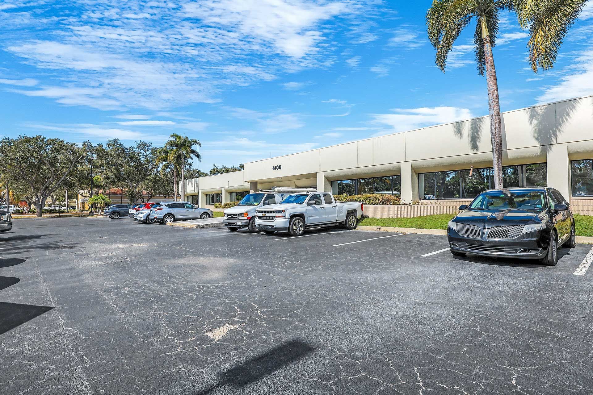 Parking lot with cars in front of a white commercial building on a sunny day.