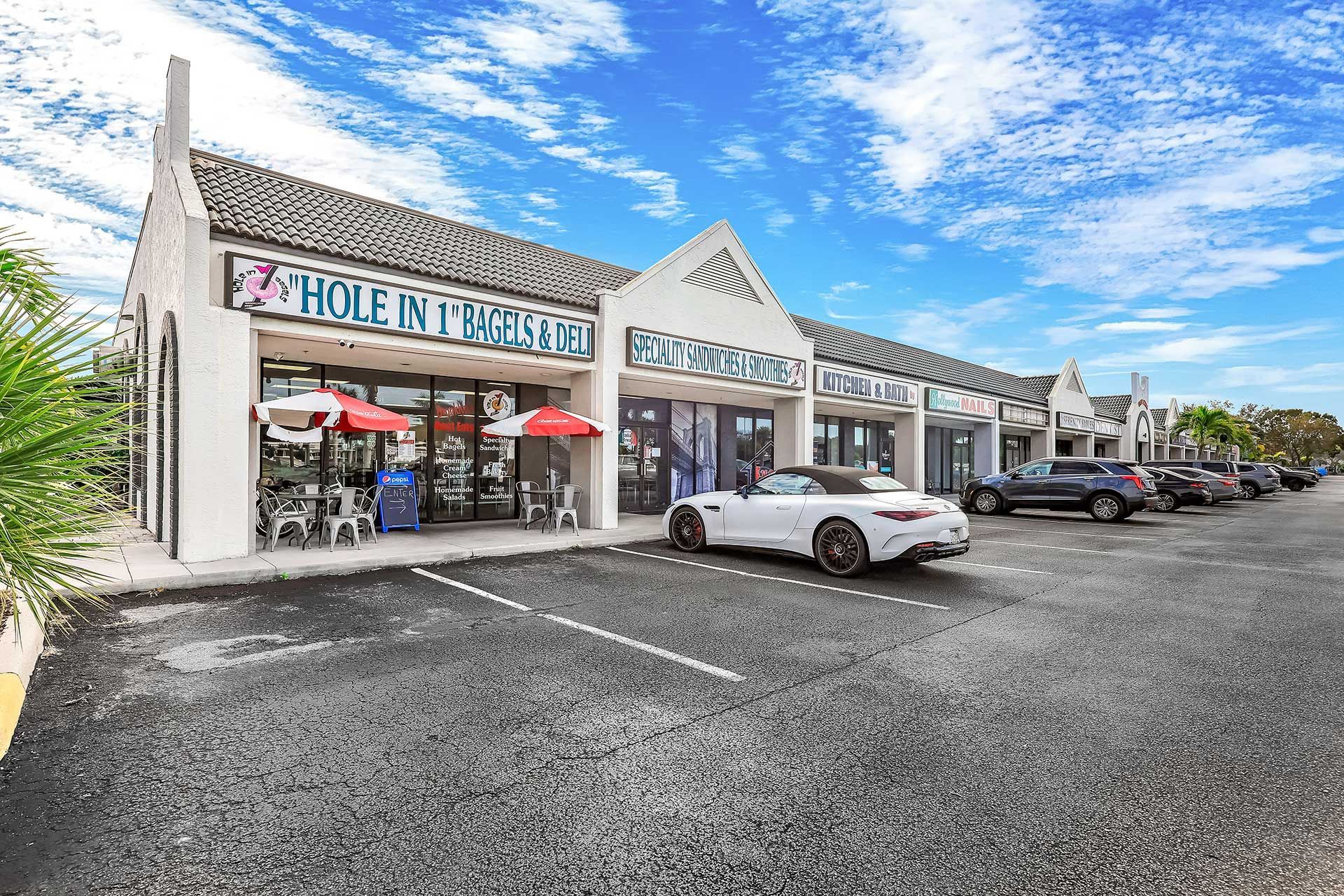 Shops in a strip mall with a car parked out front. Bright blue sky with clouds.