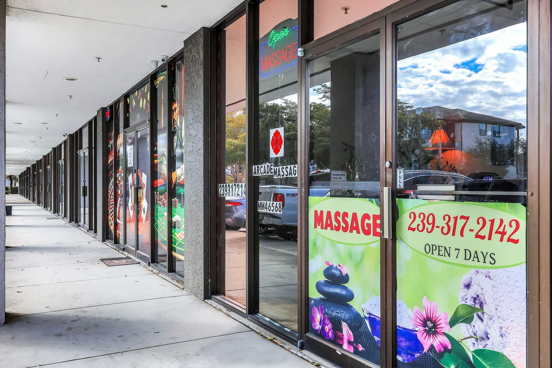 Exterior view of a strip mall with glass-fronted shops. One advertises massage services.