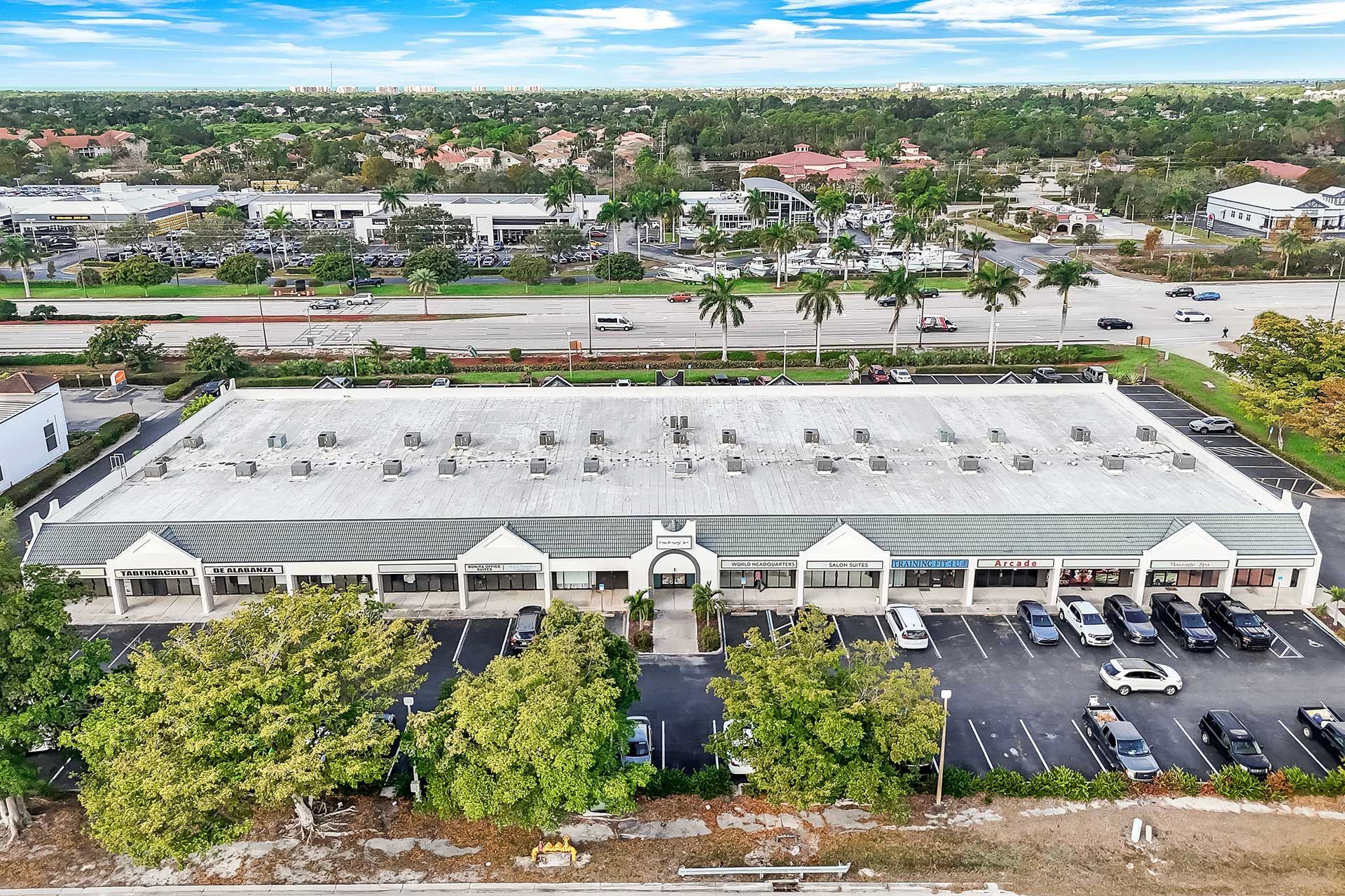 Aerial view of a long, single-story commercial building with a parking lot in a suburban area.