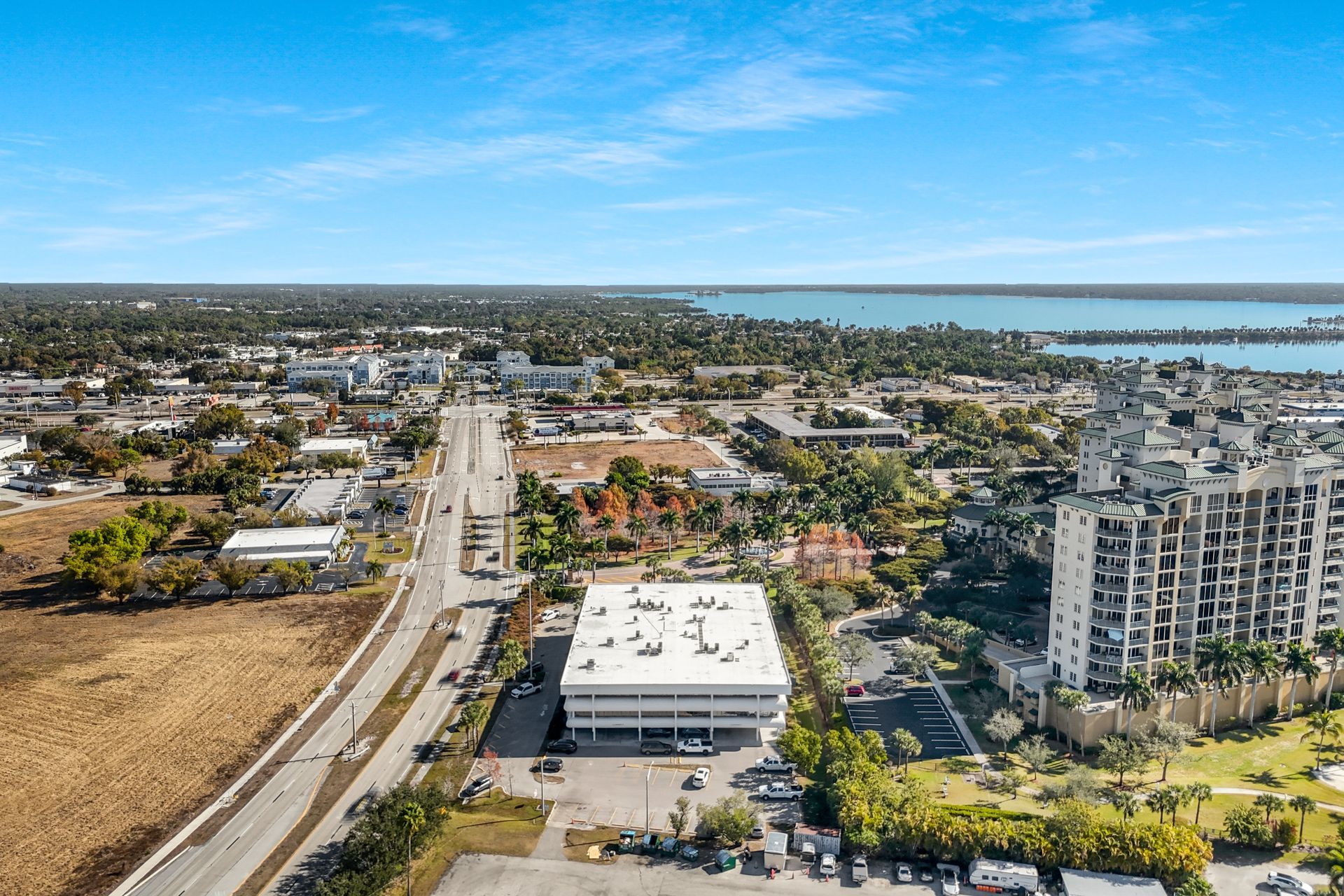 Aerial view of a town with a white building in the center, road, and waterfront in the background.