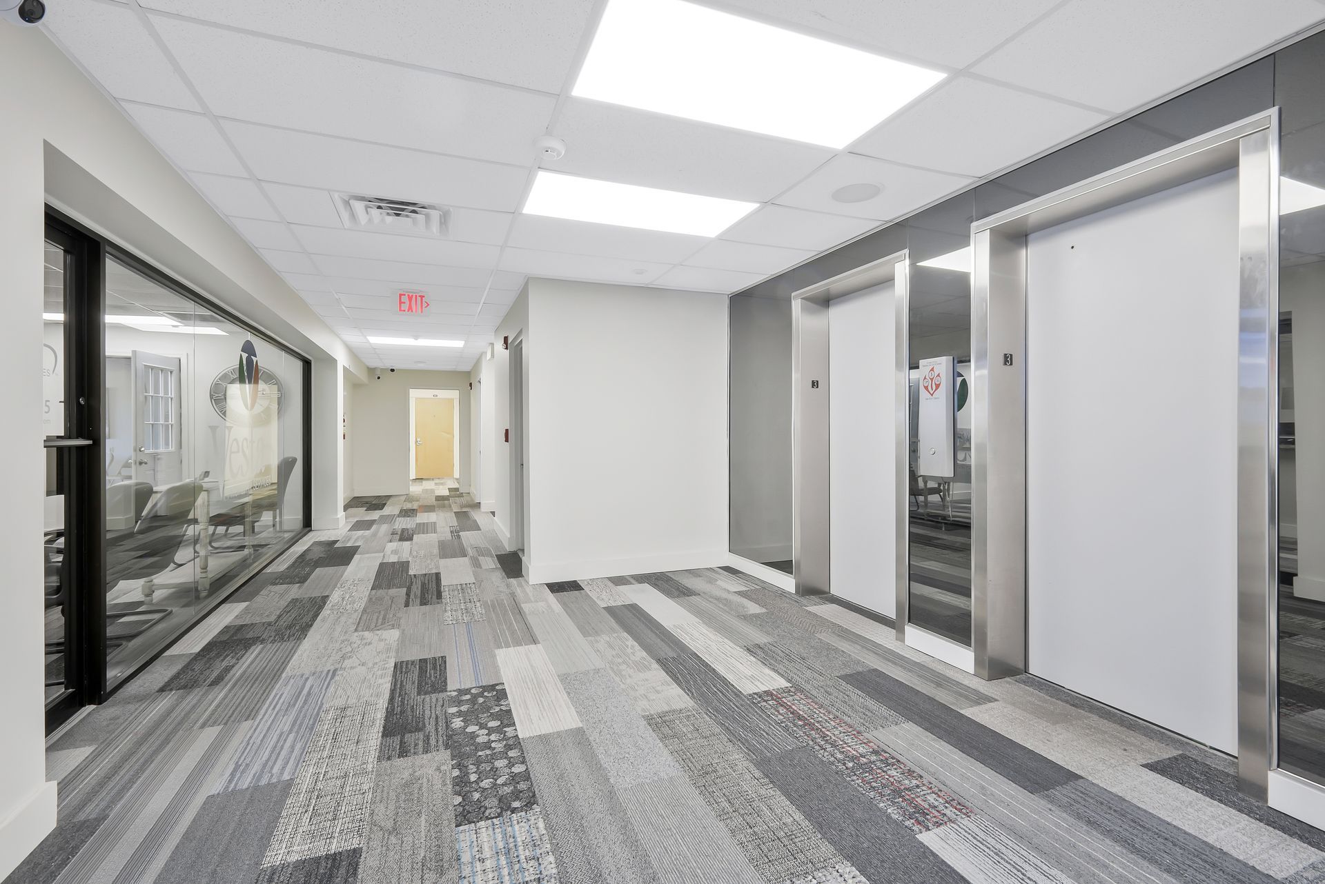 Office hallway with carpet, elevators, and glass-walled office space.
