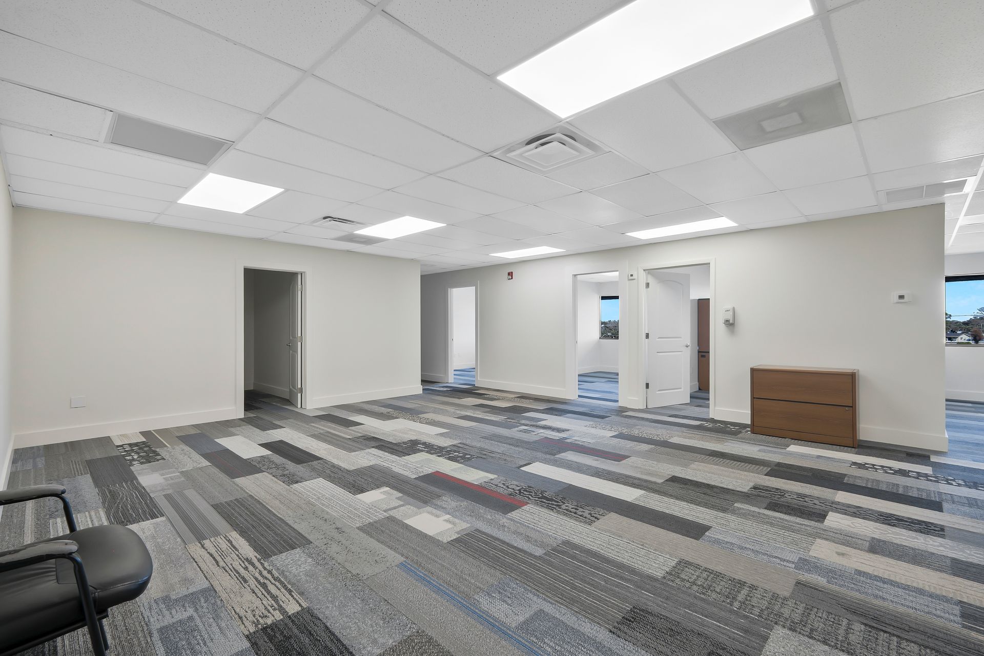 Empty office space with gray patterned carpet, white walls, and recessed lighting.