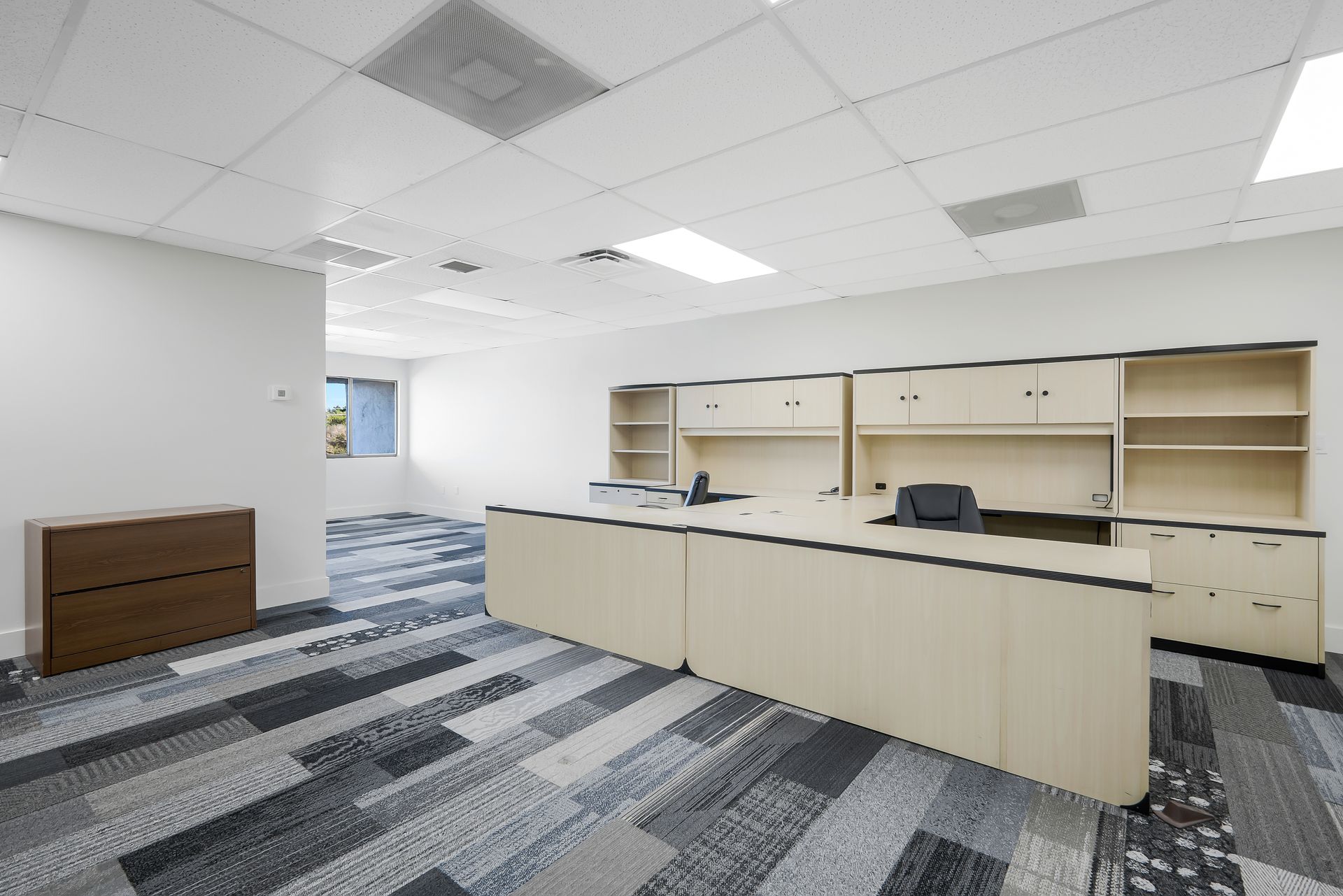 Empty office space with built-in desk, cabinets, and patterned carpet.