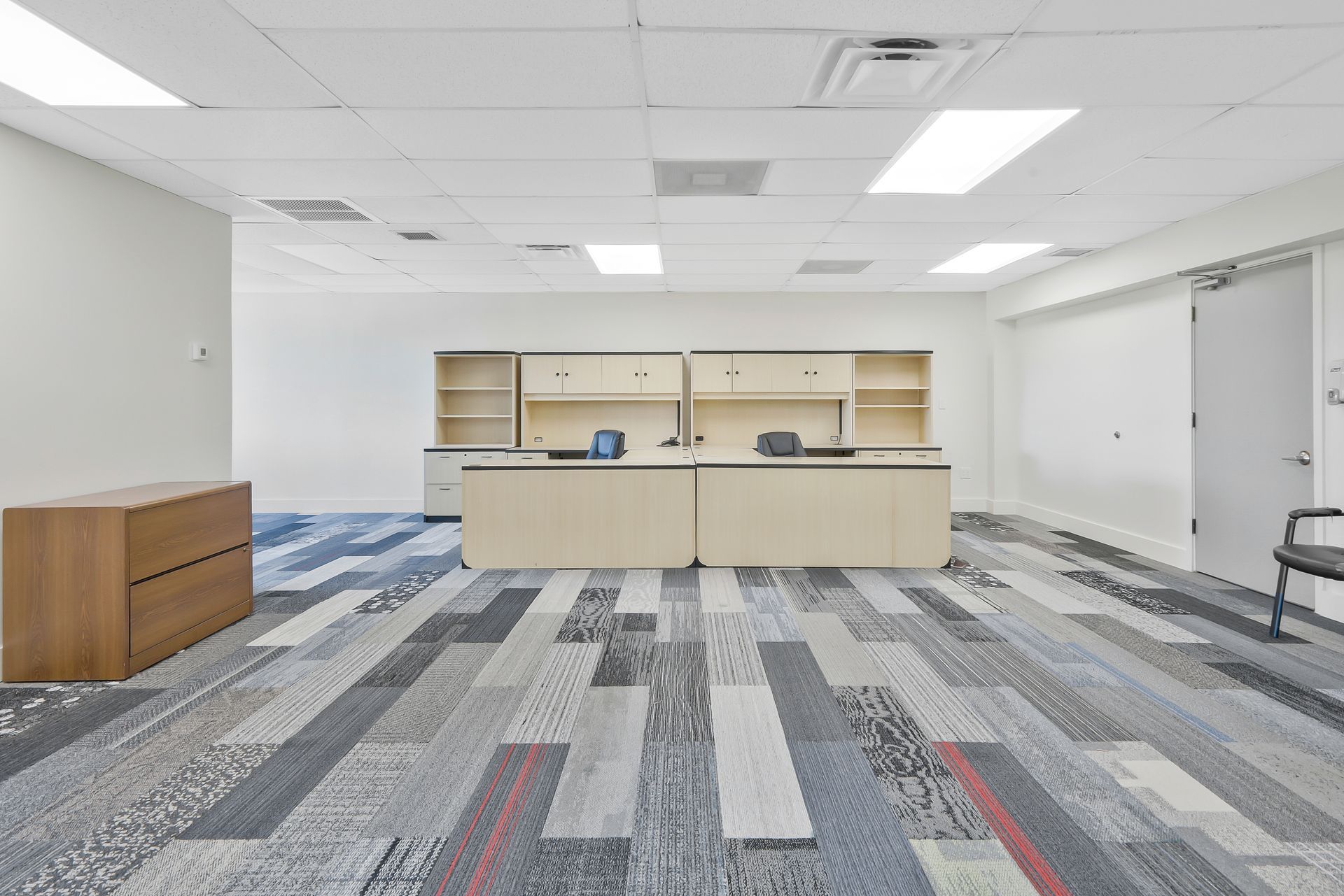 Empty office space with desks, cabinets, patterned carpet, and bright ceiling lights.