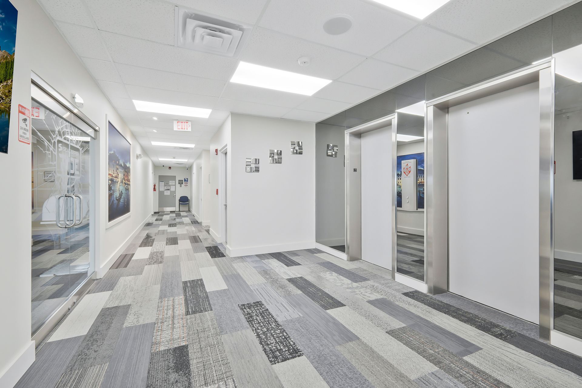 Hallway with modern design; gray and white carpet, white walls, doors, and bright overhead lights.
