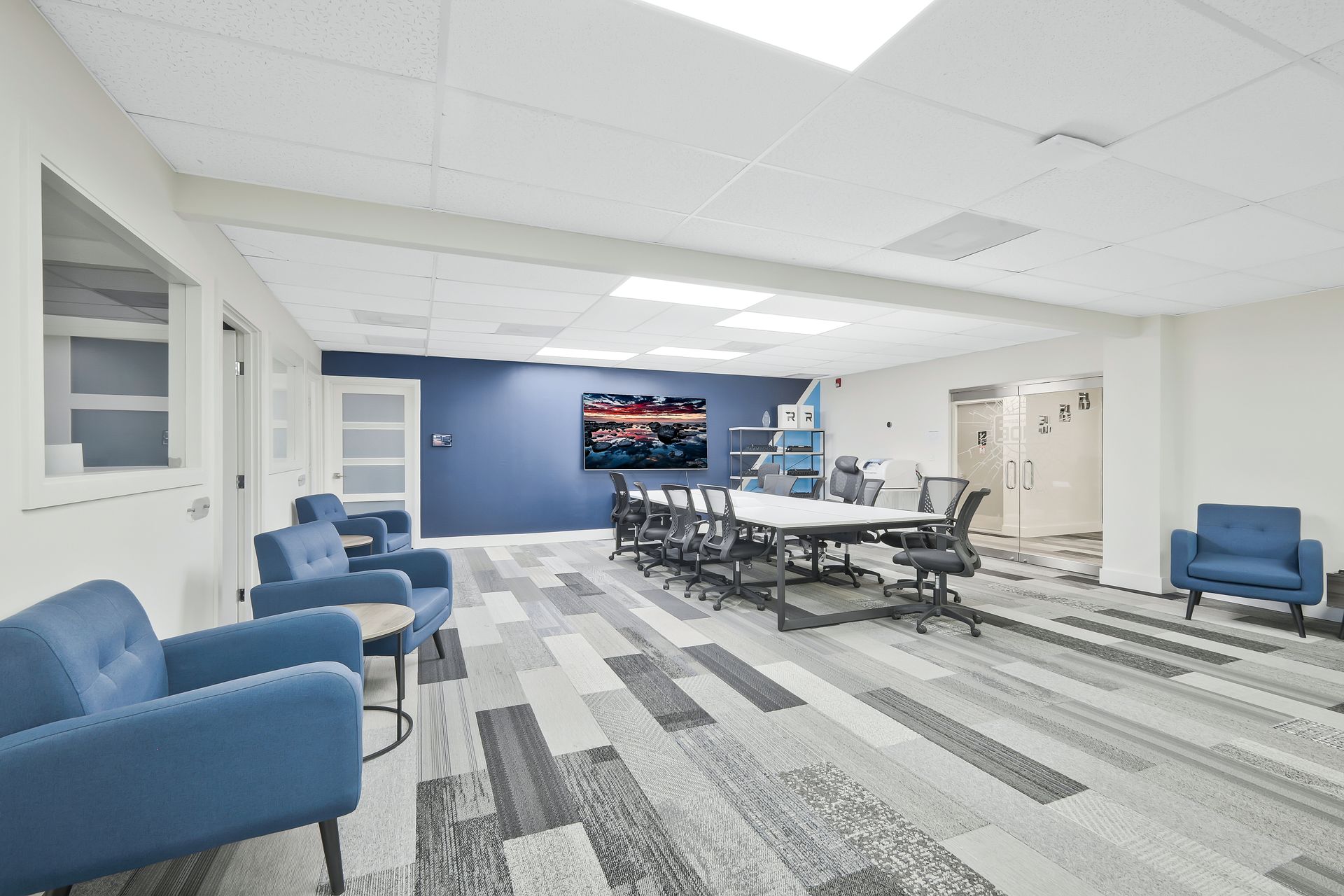 A modern office space with blue armchairs, a large conference table, and a blue accent wall.
