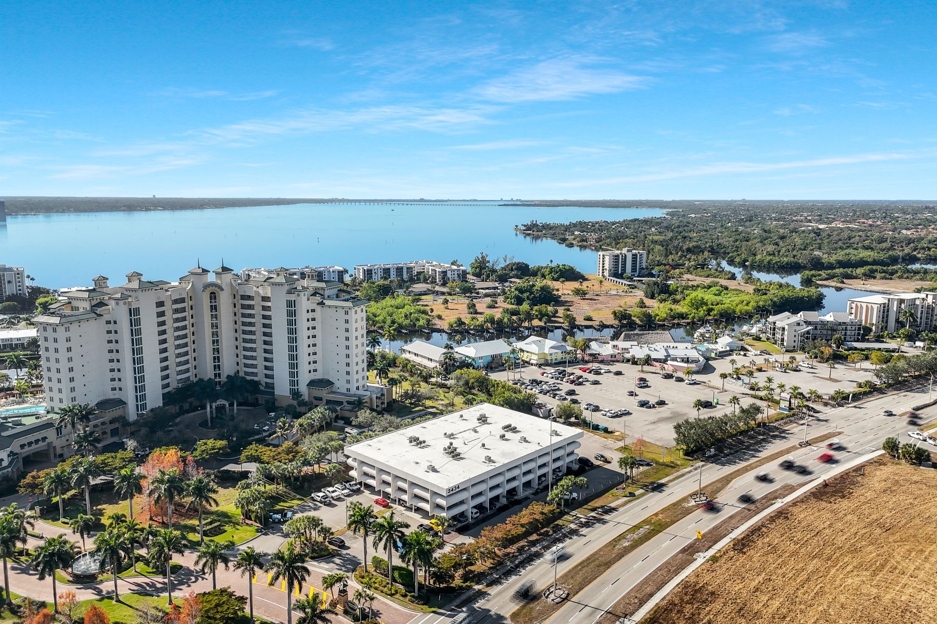Aerial view of waterfront buildings, parking, and a body of water under a blue sky.