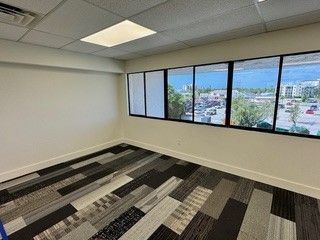 Empty office space with large windows, patterned carpet, and neutral walls.