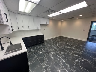 Empty office space with white and black cabinets, a stainless steel sink, and marbled tile floors.