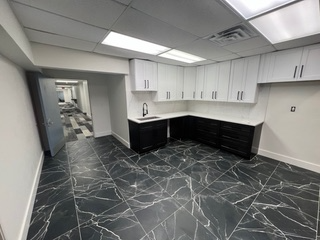 Modern kitchen with white and black cabinets, black marble-look flooring, and an open doorway.