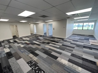 Empty office space with patterned carpet and fluorescent lighting. White walls, doors, and a window.