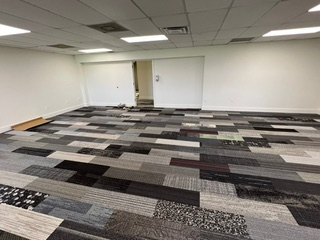 Room with newly installed multi-colored carpet tiles; white walls, recessed ceiling lights, and open doorway.