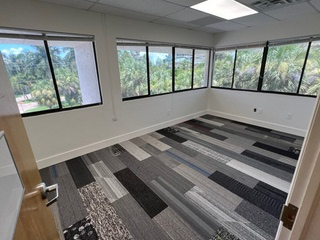 Empty office room with gray, black, and white patterned carpet, windows, and bright outdoor views.