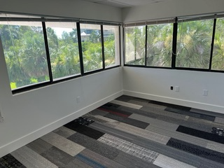 Empty room with large windows overlooking trees; multi-colored plank flooring.