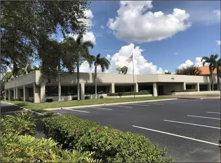 Office building with palm trees, American flag, and blue sky.