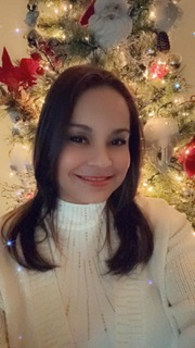 Woman smiling in front of a decorated Christmas tree, wearing a white sweater.