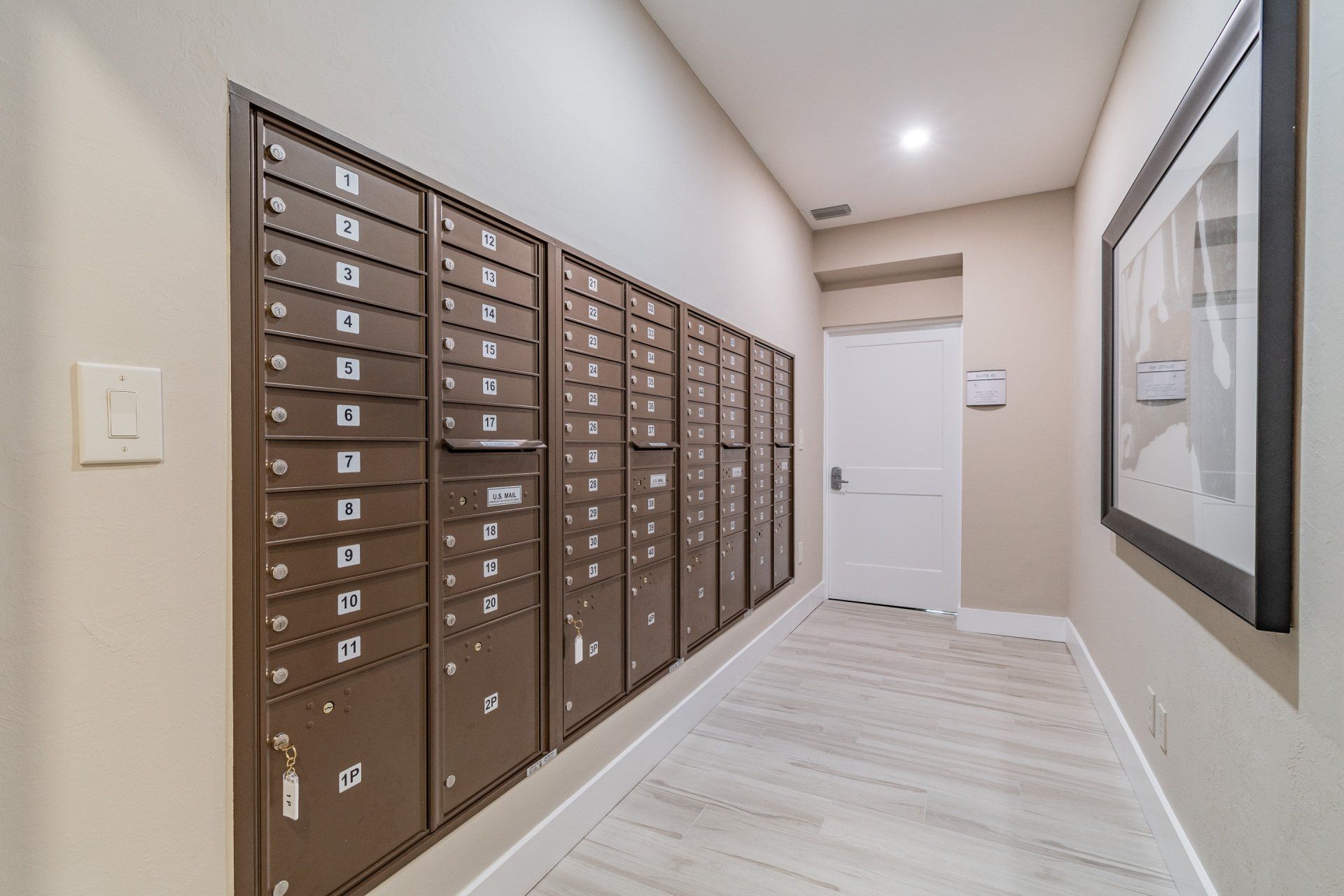 Mailboxes in a hallway, tan wall with artwork, and a white door in the distance.