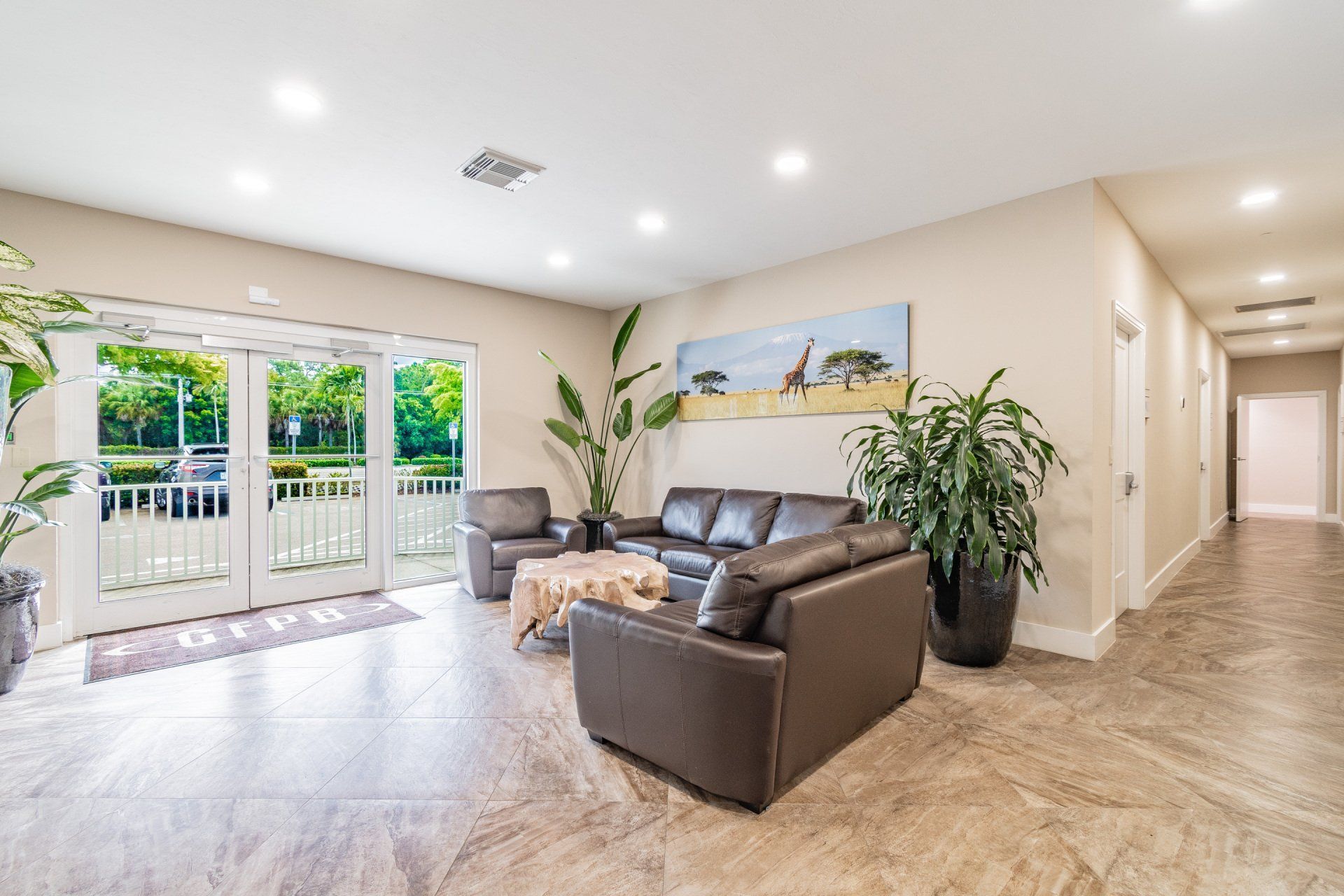 Lobby with brown leather seating, large windows, and a hallway. Plants and artwork decorate the space.