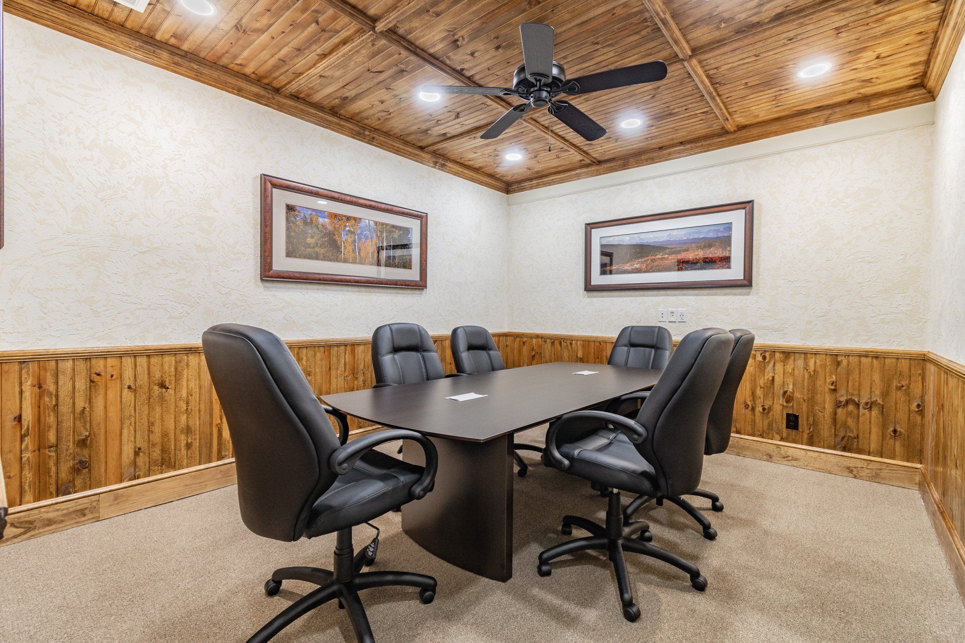 Conference room with black chairs around a table, wooden paneling, art on walls.