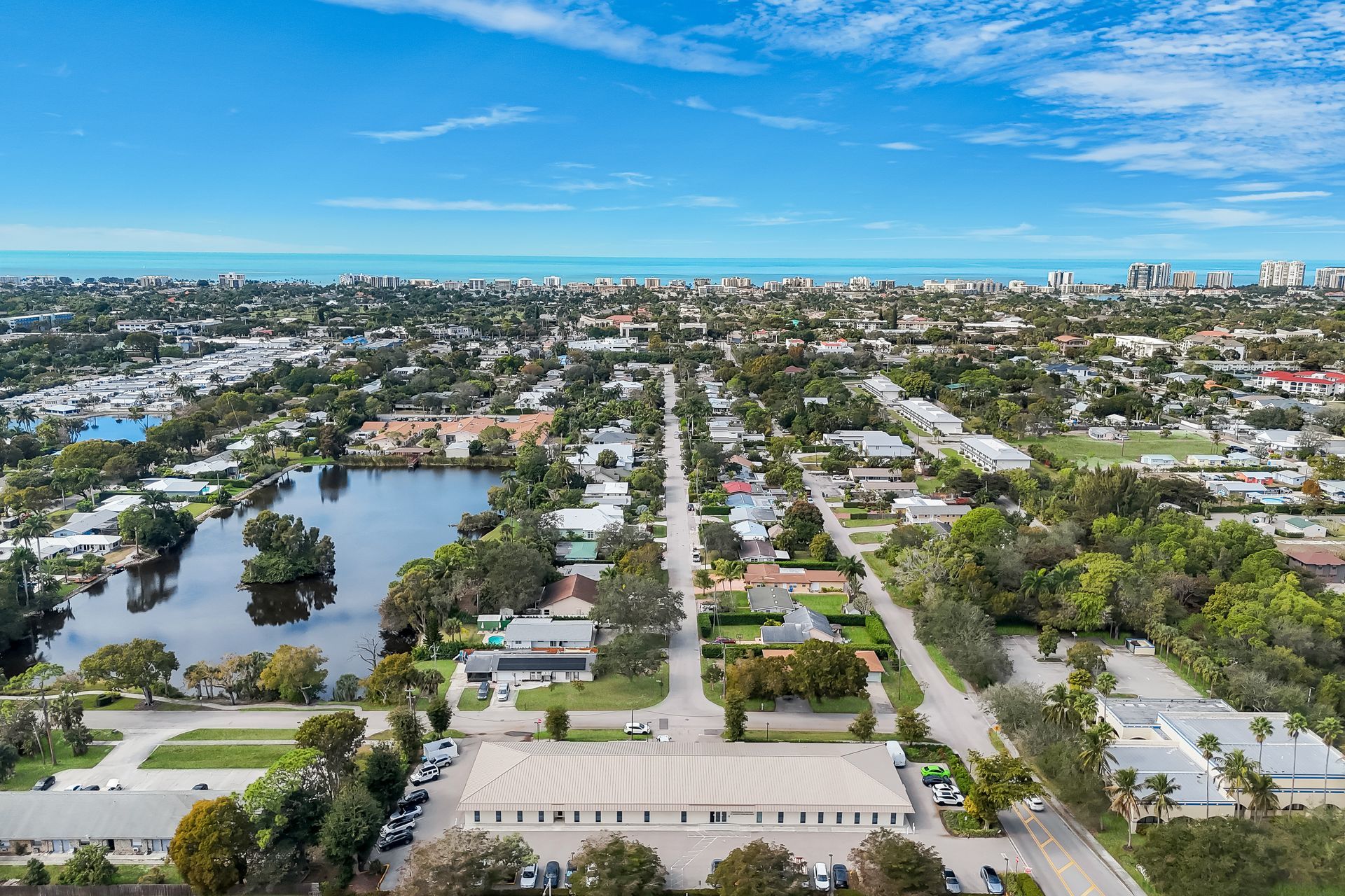 Aerial view of a town with a lake and ocean in the distance under a blue sky.