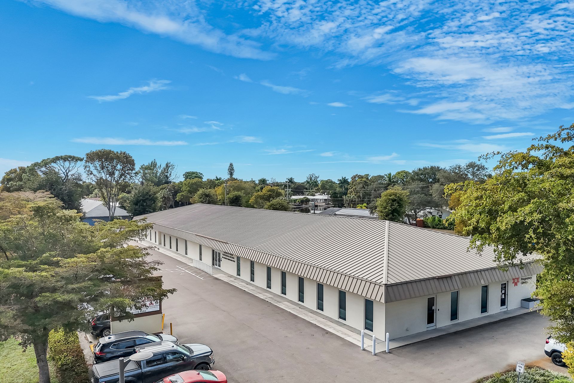 Long, white commercial building with rows of windows and a parking lot, under a blue sky.