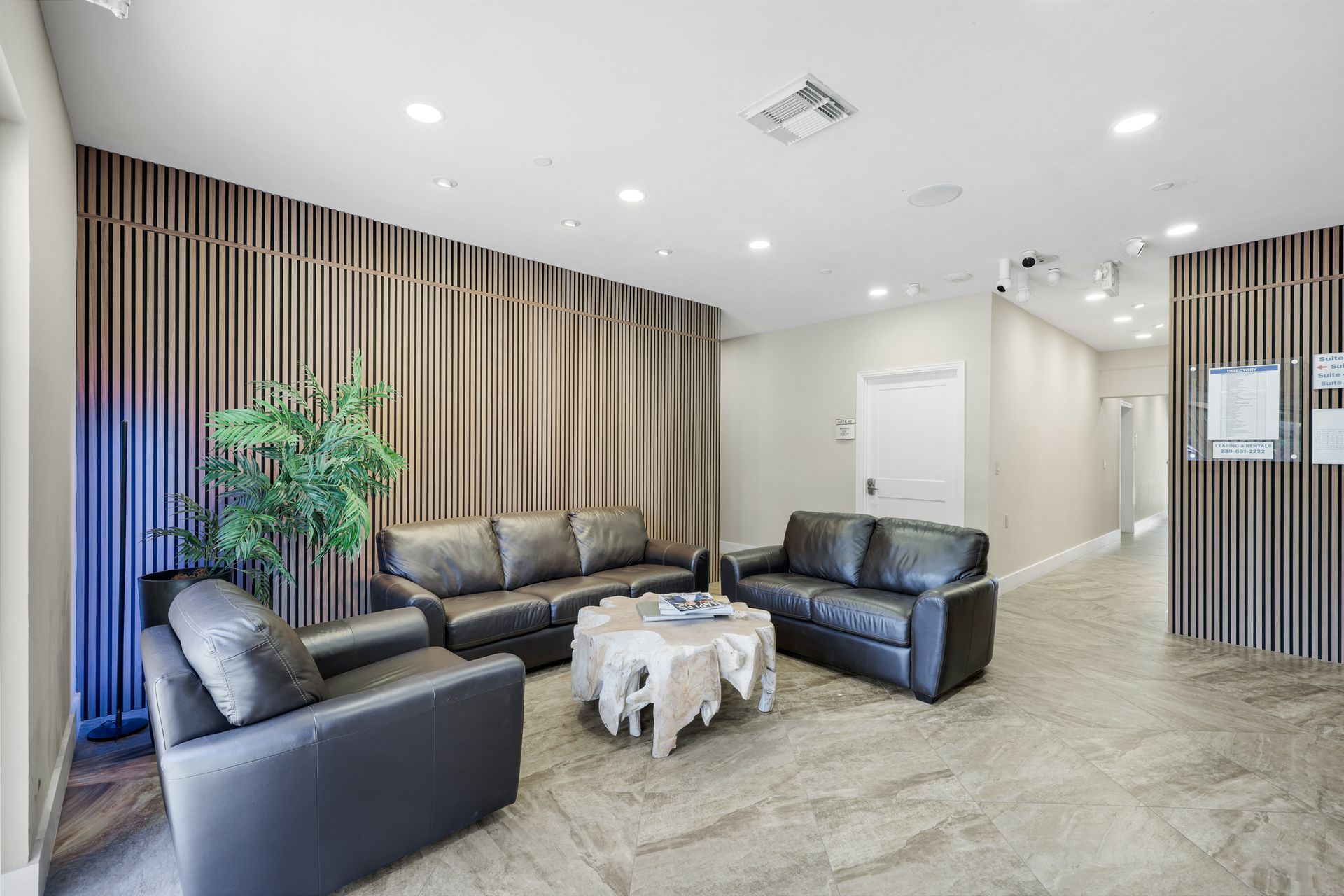 Lobby with three black leather couches, a coffee table, and wood paneling on the walls.