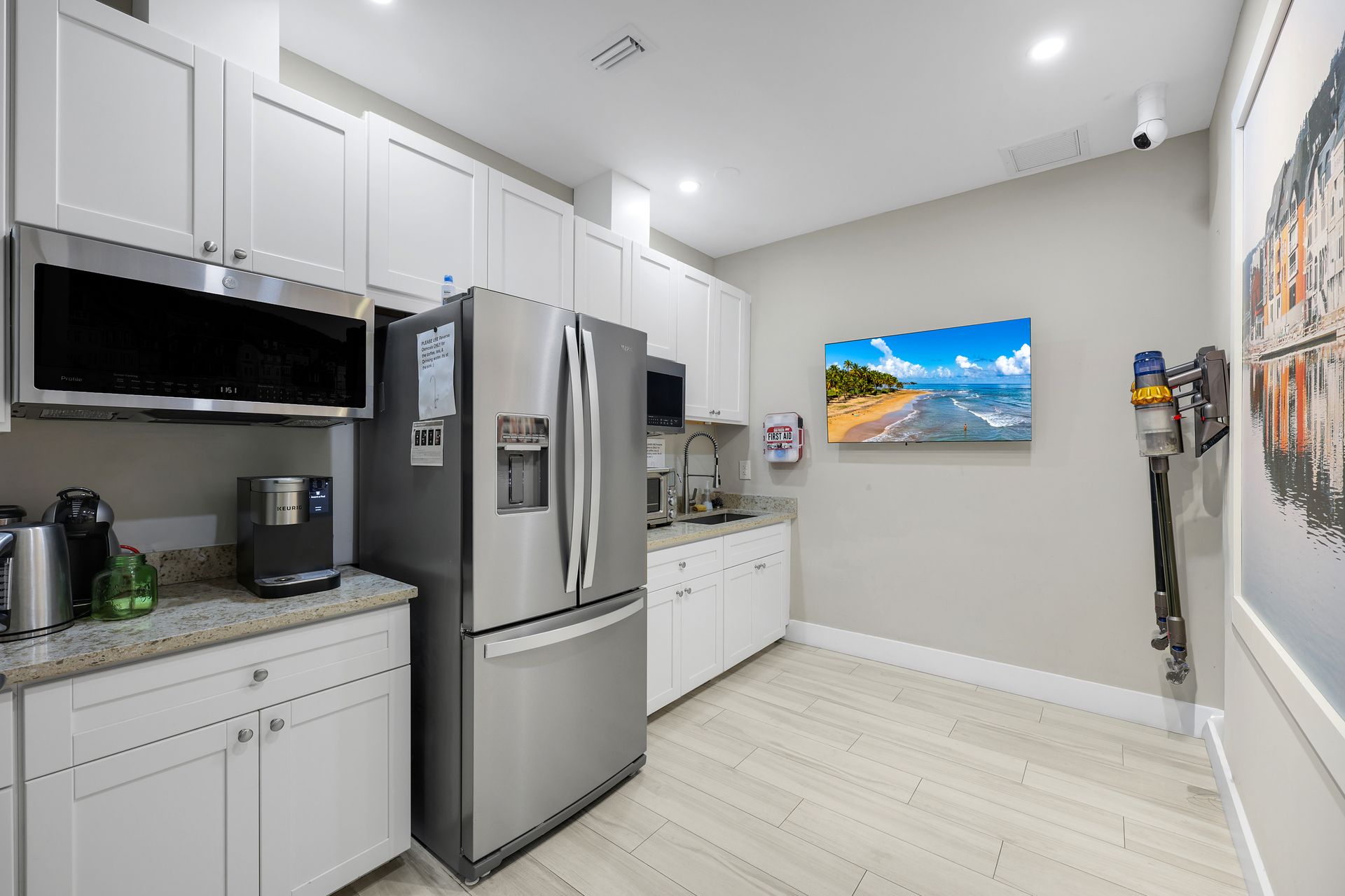 Modern kitchen with stainless steel appliances, white cabinets, and a beach scene on the wall.