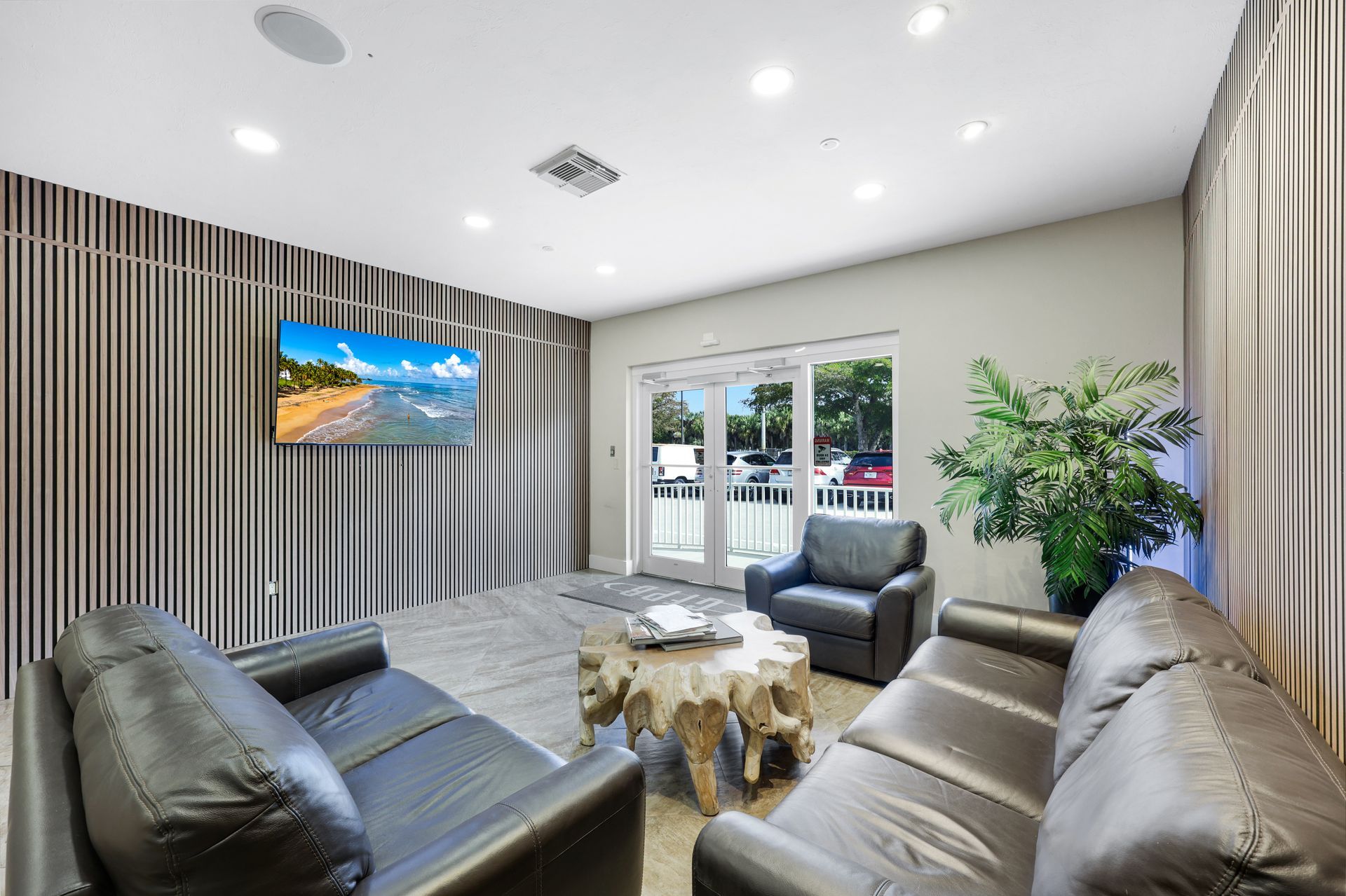 Lounge area with gray leather sofas, a TV, and a wooden coffee table in front of glass doors.