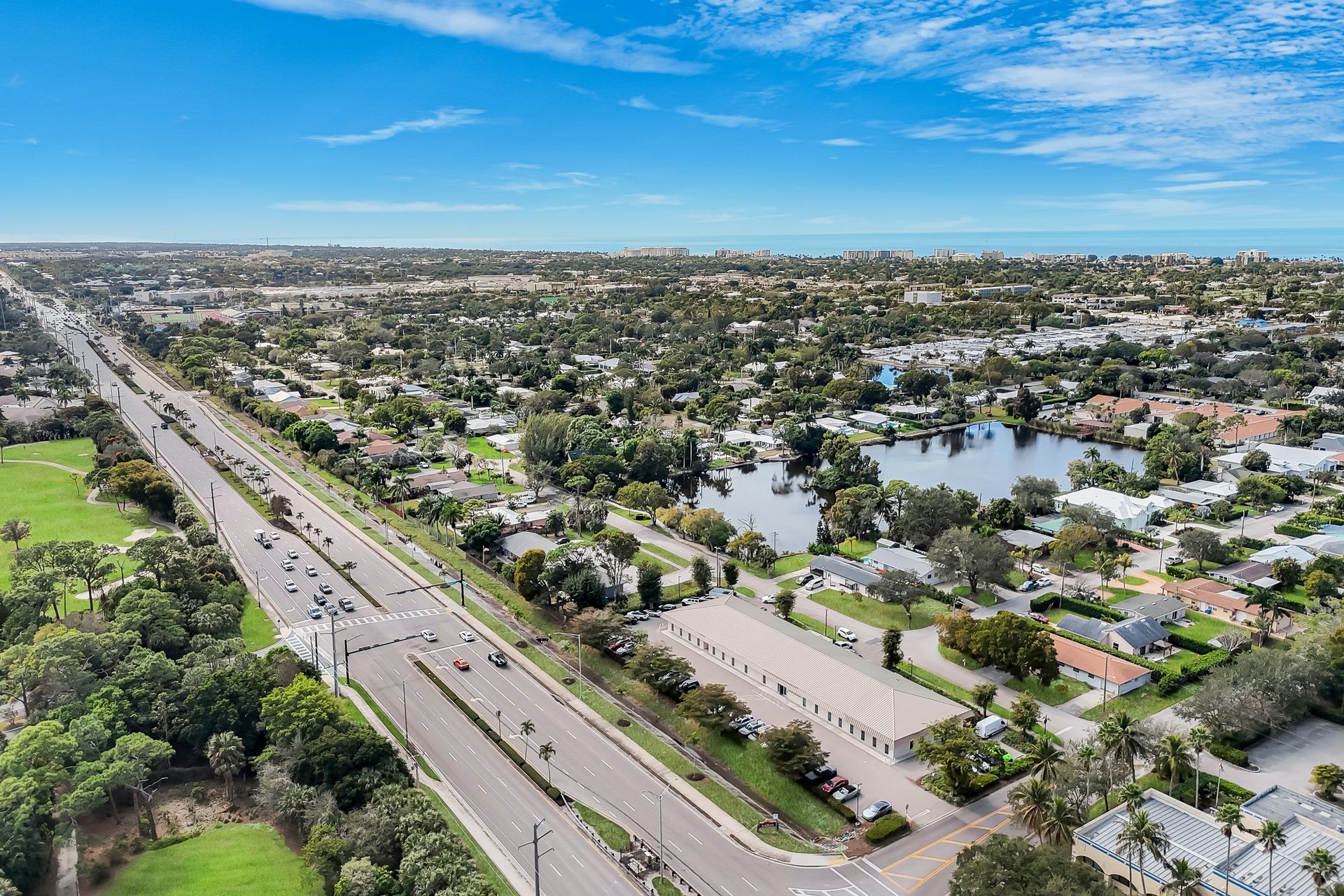 Aerial view of a suburban neighborhood with a highway, houses, and a lake under a blue sky.