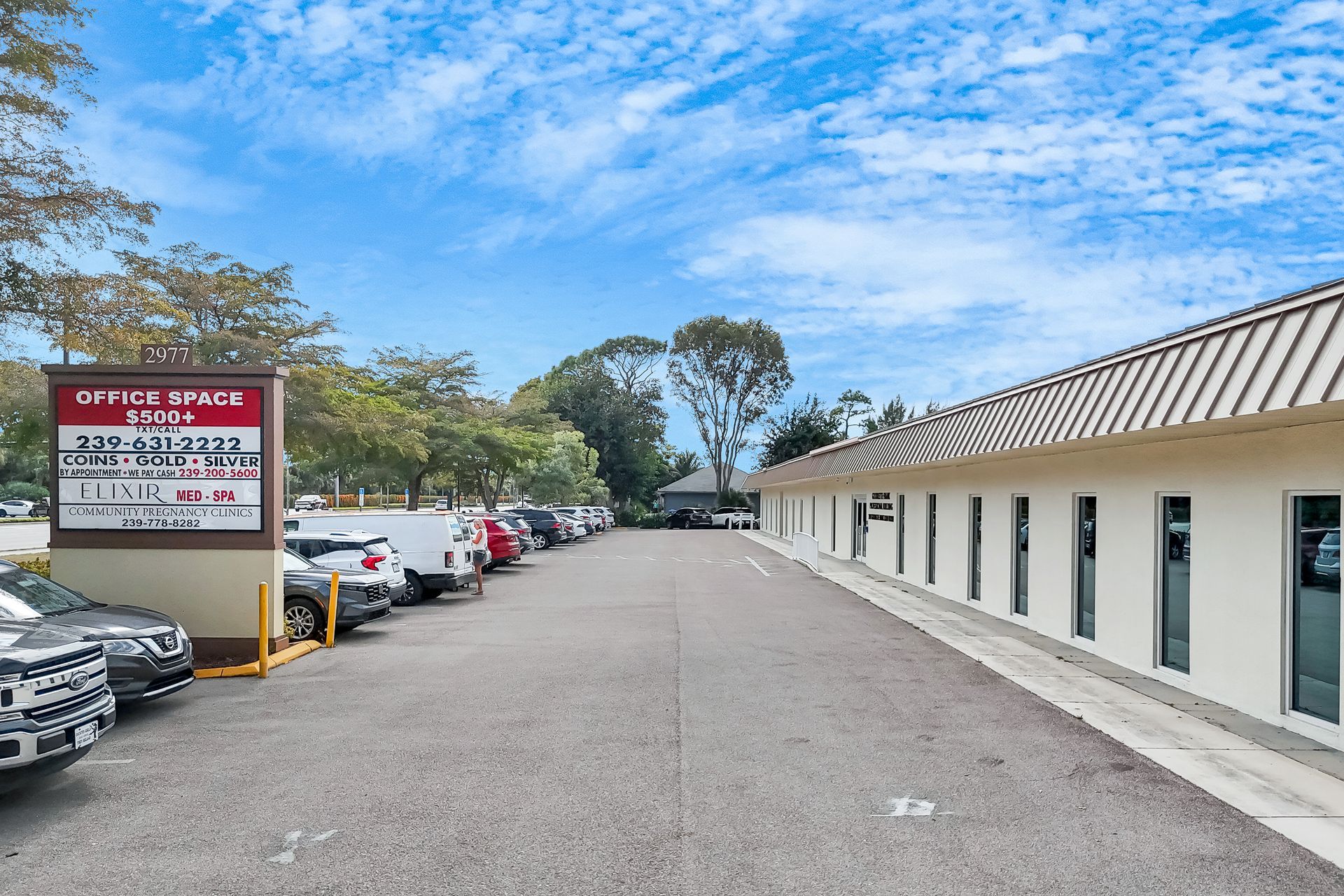 Parking lot in front of a beige office building with a sign that says