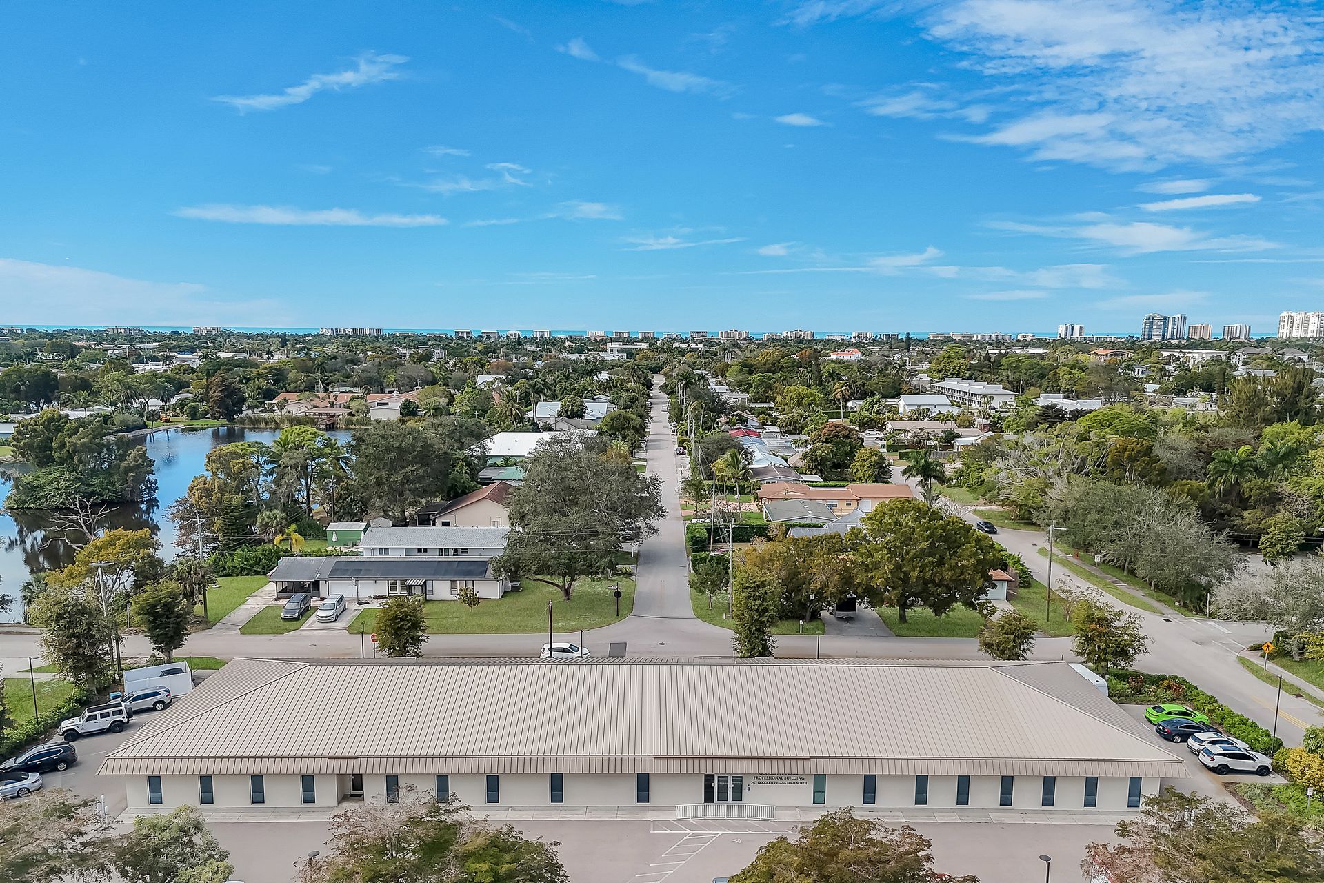 An aerial view of a building with a curved roof, street, and suburban homes under a blue sky.