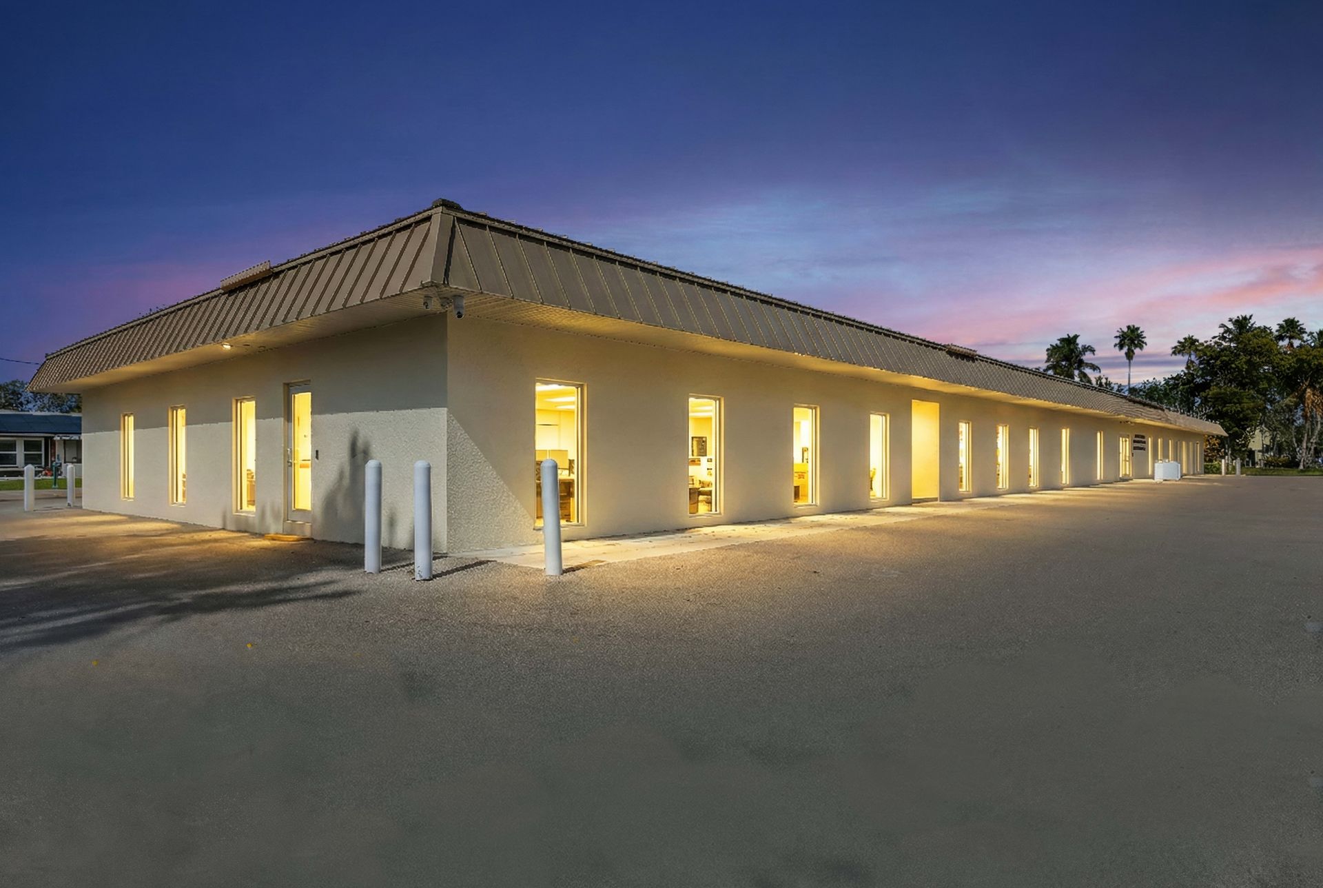 A single-story commercial building with illuminated windows against a twilight sky.
