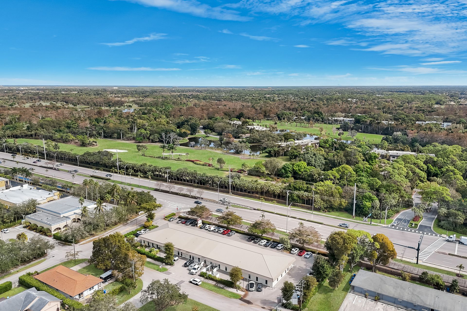 Aerial view of a road, businesses, and a golf course, under a blue sky.