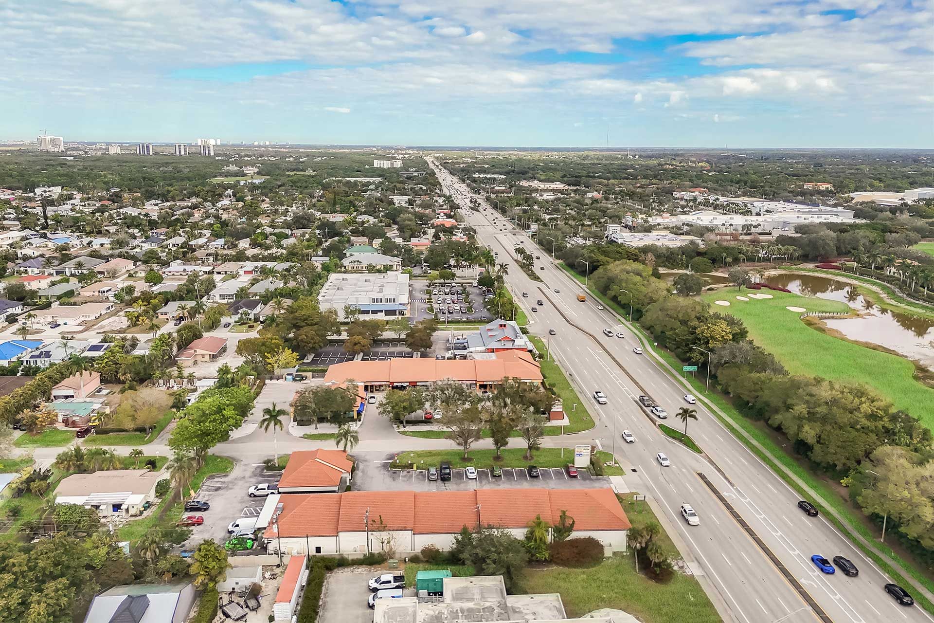 Aerial view of a suburban area with a multilane highway, houses, commercial buildings, and a golf course.