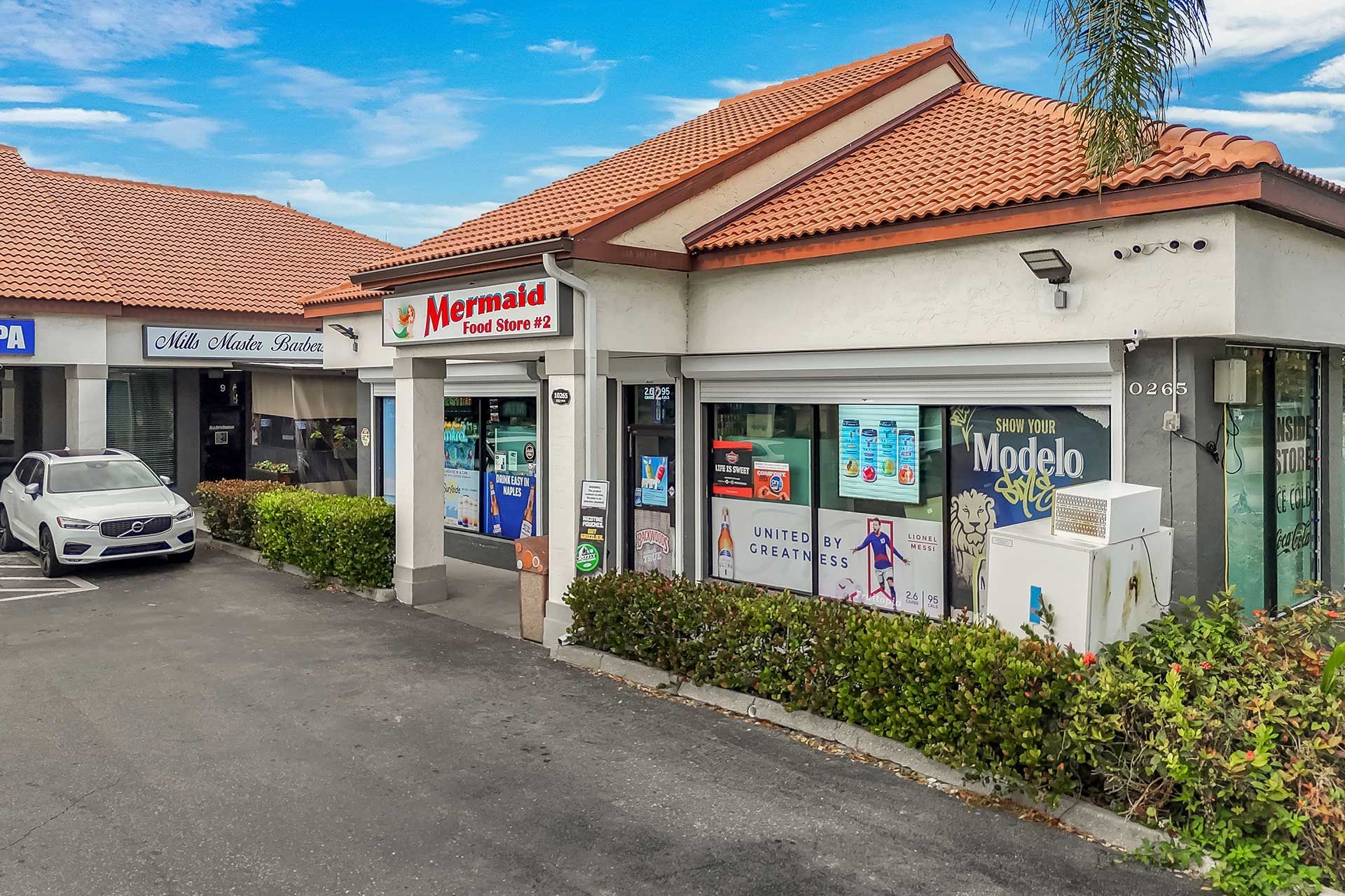 Exterior of a strip mall with shops, a white SUV, and blue sky. Herrera store is in focus.